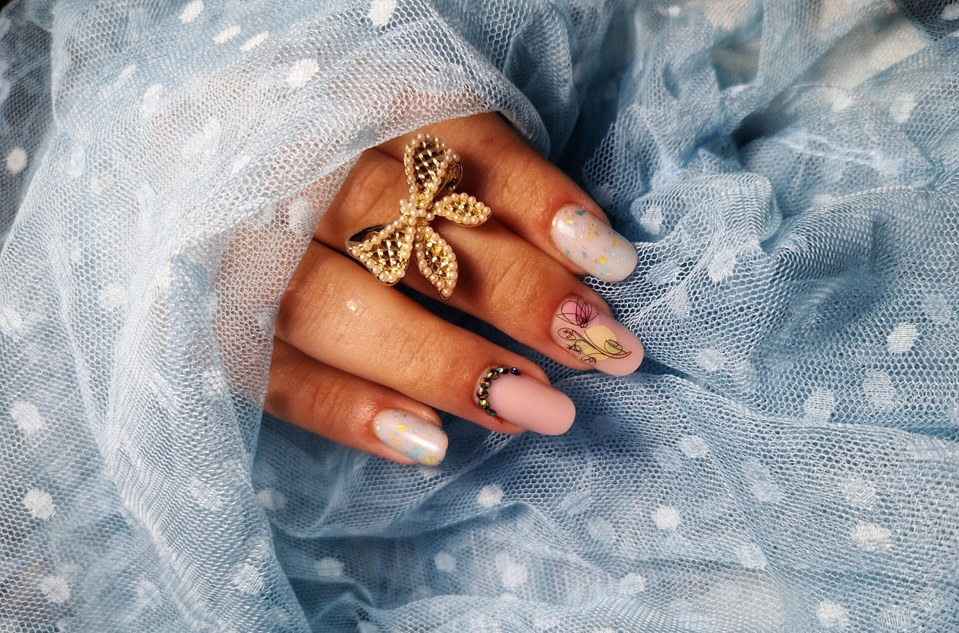 Elegant spring nail art featuring nude pink base, delicate floral detail, and glitter accents